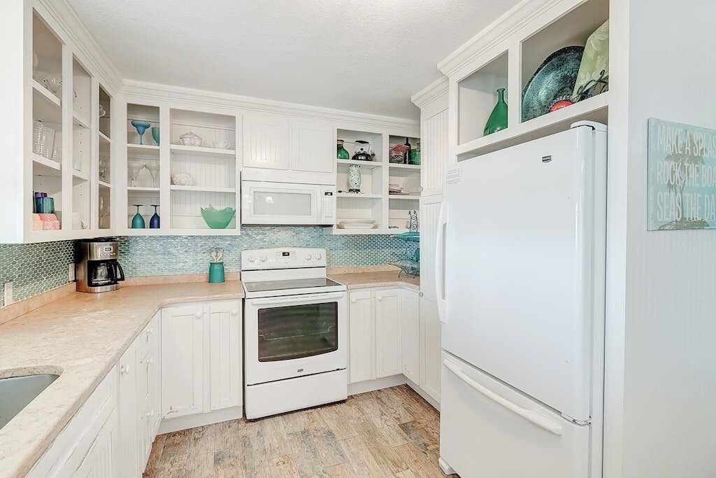 A kitchen with white cabinets, a stove, a refrigerator, and a microwave.