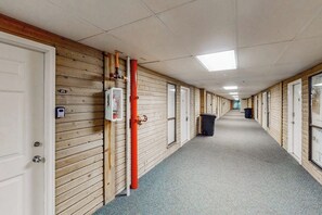 A corridor with wooden walls, doors, and a trash bin. - Seawall Getaway - Pool, Balcony, Walk to Beach (Galveston)
