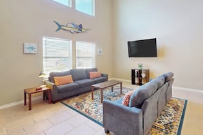 A living room with a grey sofa, a coffee table, a TV mounted on the wall, and a patterned rug. - The Blue House by Whitecap Beach (Corpus Christi)