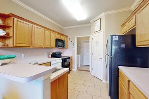 A kitchen with wooden cabinets, a microwave, a refrigerator, and a dishwasher. - The Blue House by Whitecap Beach (Corpus Christi)