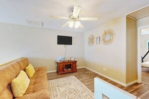 A living room with a ceiling fan, a flat-screen TV, a wooden cabinet, and decorative wall art. - The Blue House by Whitecap Beach (Corpus Christi)