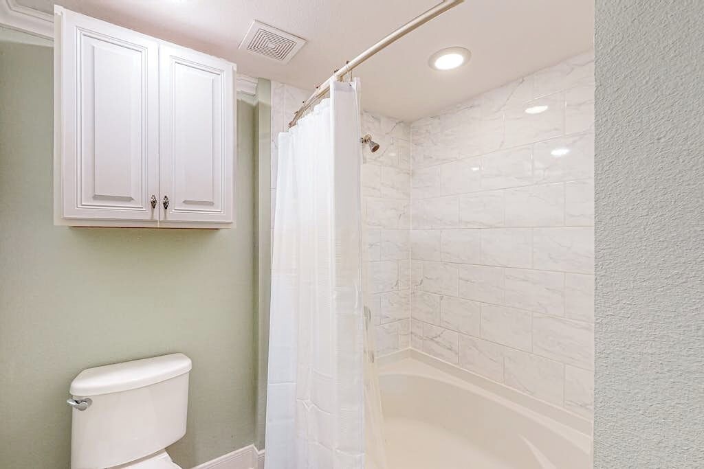 A bathroom with a toilet, a shower with a curtain, and a bathtub.