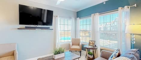 Una sala moderna con televisor de pantalla plana, ventilador de techo y ventanas amplias con cortinas.