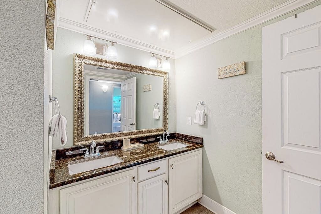 Un baño con tocador doble, un espejo grande con marco dorado y una puerta blanca.