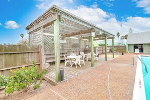 A covered outdoor seating area with a pool, wooden deck, and a fenced backyard. - Puente Vista 147 - Waterfront, Pool & Dock (Corpus Christi)