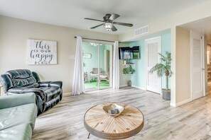 A living room with a leather sofa, a round coffee table, a ceiling fan, a television, and a sliding glass door leading to a balcony. - Puente Vista 147 - Waterfront, Pool & Dock (Corpus Christi)