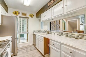 A kitchen with white cabinets, a countertop, and a window with blinds. - Puente Vista 147 - Waterfront, Pool & Dock (Corpus Christi)