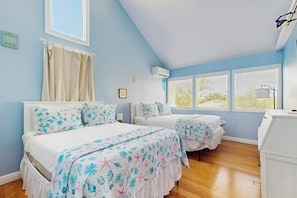Een slaapkamer met twee bedden, een raam, een plafondventilator en een witte dressoir.