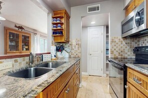 Eine Küche mit Granit Arbeitsplatten, Edelstahlgeräten, Holzschränken und einer gefliesten Spritzschutzwand.