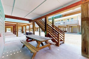 A covered outdoor area with wooden picnic tables and a staircase. - Ocean Village 18 Sea Ya Soon (Port Aransas)