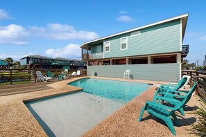 A swimming pool with lounge chairs, a wooden deck, and a building with a balcony. - Ocean Village 18 Sea Ya Soon (Port Aransas)