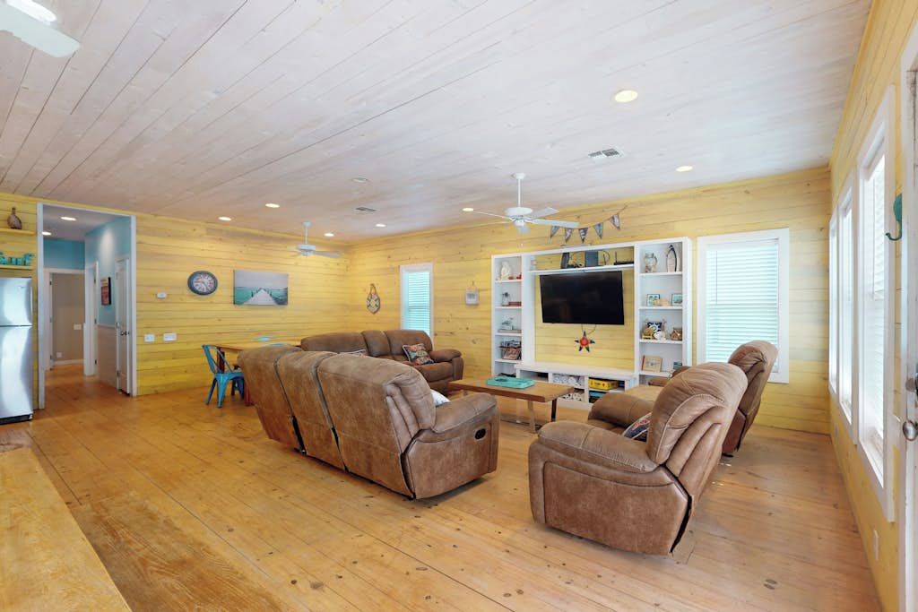 Ein Wohnzimmer mit Holzboden, einer Sofagarnitur, einem Fernseher und einem Deckenventilator.