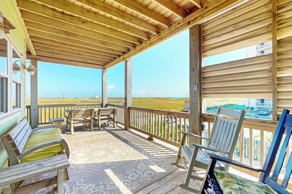 A covered outdoor area with wooden furniture and a view of the beach.