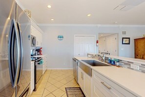 A modern kitchen with white cabinetry, a stainless steel refrigerator, a built-in oven, and a large island with a sink. - Gulf Breezes Unit B - Pool, Fenced Yard & Dogs OK (Port Aransas)
