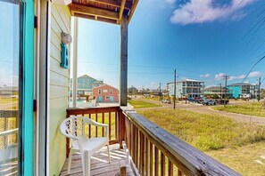A wooden deck with a white plastic chair, overlooking a street with buildings and a clear sky. - Gulf Breezes Unit B - Pool, Fenced Yard & Dogs OK (Port Aransas)