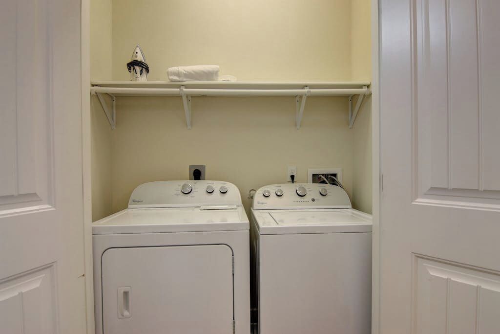 A laundry room with two white front-loading washing machines and a shelf above them.