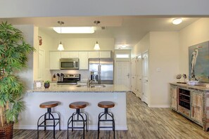 A kitchen with white cabinets, stainless steel appliances, and a bar area with stools. - Nemo Cay 15106 - Pool, Patio, Sleeps 10, Dogs OK (Corpus Christi)