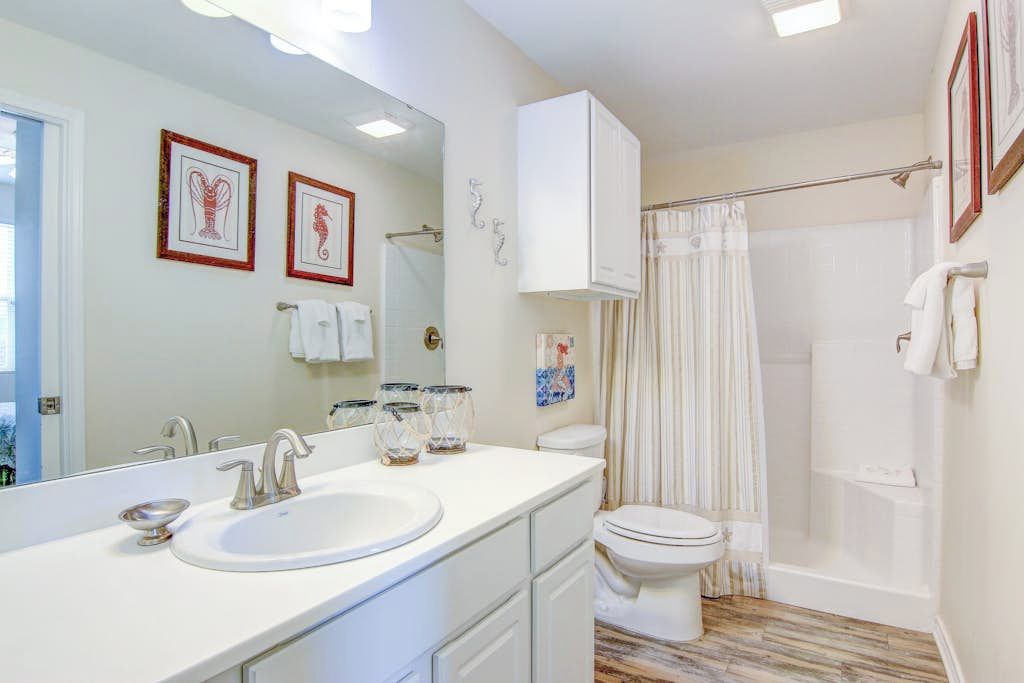 A bathroom with a white sink, a toilet, a shower with a curtain, and framed artwork on the wall.