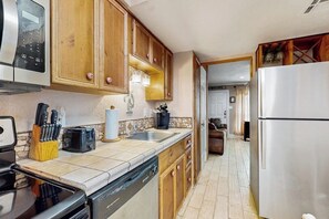 A kitchen with wooden cabinets, stainless steel appliances, a dishwasher, and a countertop with various utensils. - Quaint Oasis - Shared Pool & Beach Access (Corpus Christi)