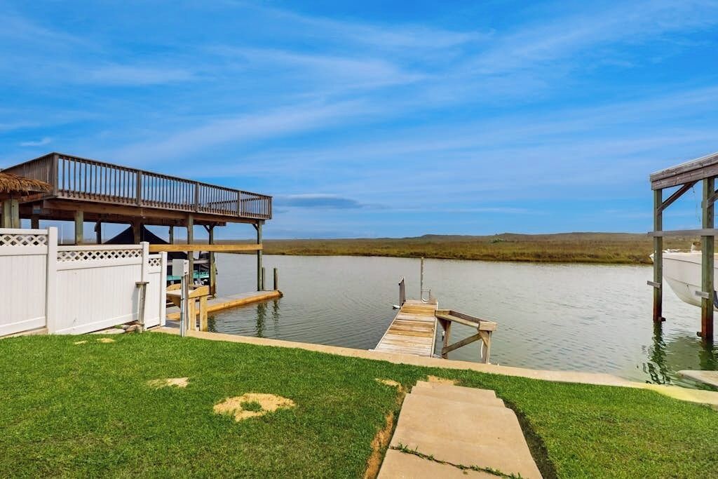 A waterfront property with a dock, a covered area, and a grassy lawn.