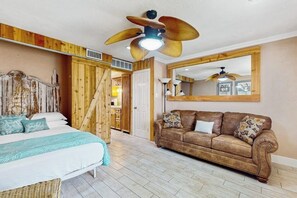 A bedroom with a bed, a wooden wardrobe, a brown leather sofa, a ceiling fan, and a large mirror. - Quaint Oasis - Shared Pool & Beach Access (Corpus Christi)