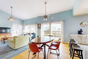 A modern living room with a sofa, a dining table with chairs, and a kitchen area with a bar. - Lost Colony Seahorse Villa (Port Aransas)