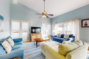 A living room with a blue sofa, a yellow sofa, a wooden coffee table, and a ceiling fan. - Lost Colony Seahorse Villa (Port Aransas)