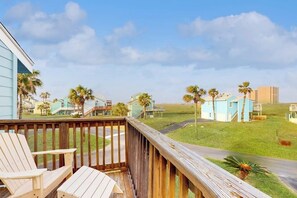 A wooden deck with chairs, a view of a coastal area with houses and palm trees, and a clear sky. - Lost Colony Seahorse Villa (Port Aransas)