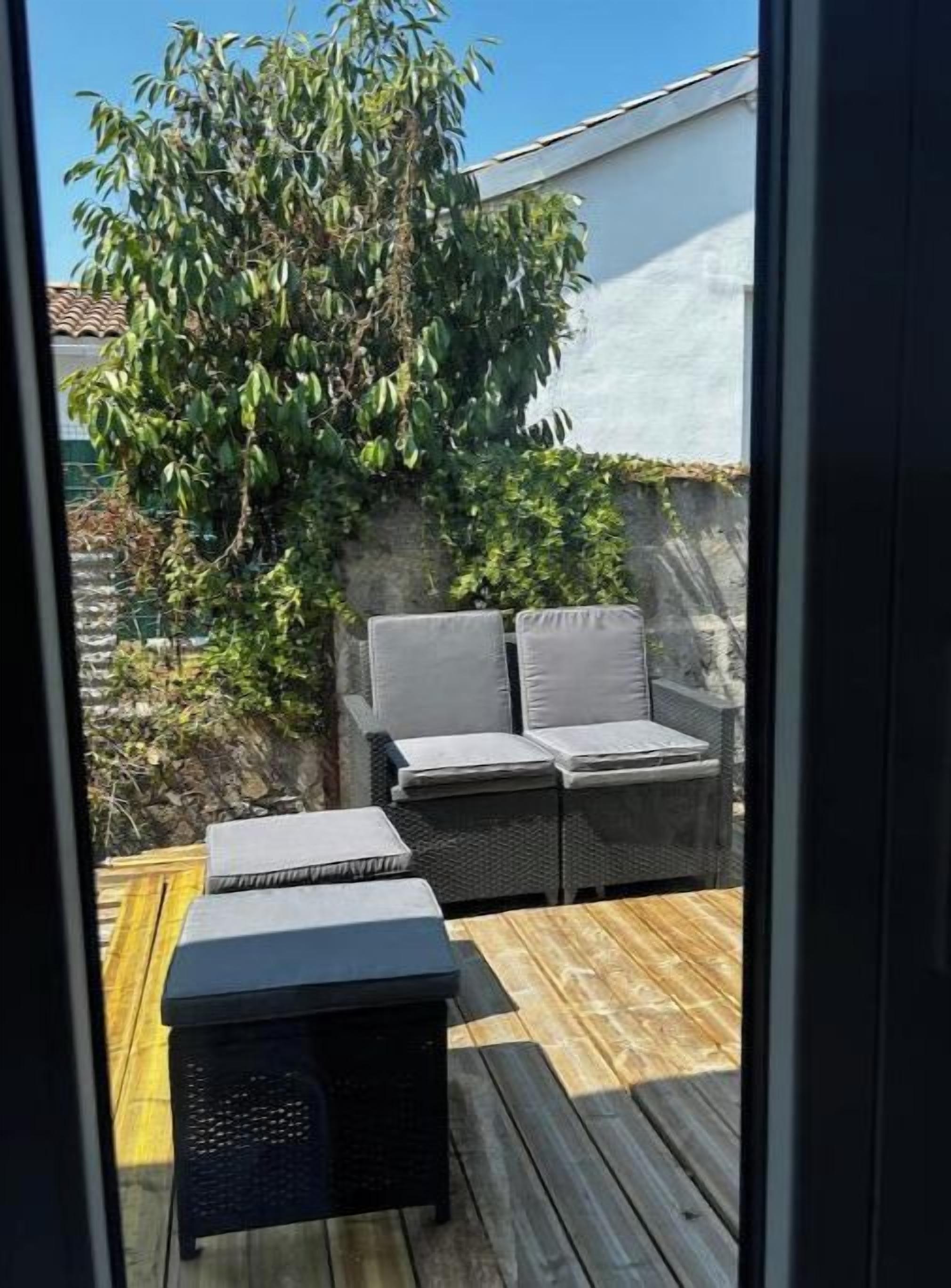 Een terras met een bank en twee kleine tafels, een houten vlonder en een boom.