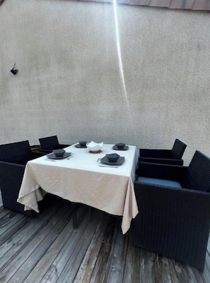 Een terras met een eettafel voor vier personen, omringd door donkere rieten stoelen.