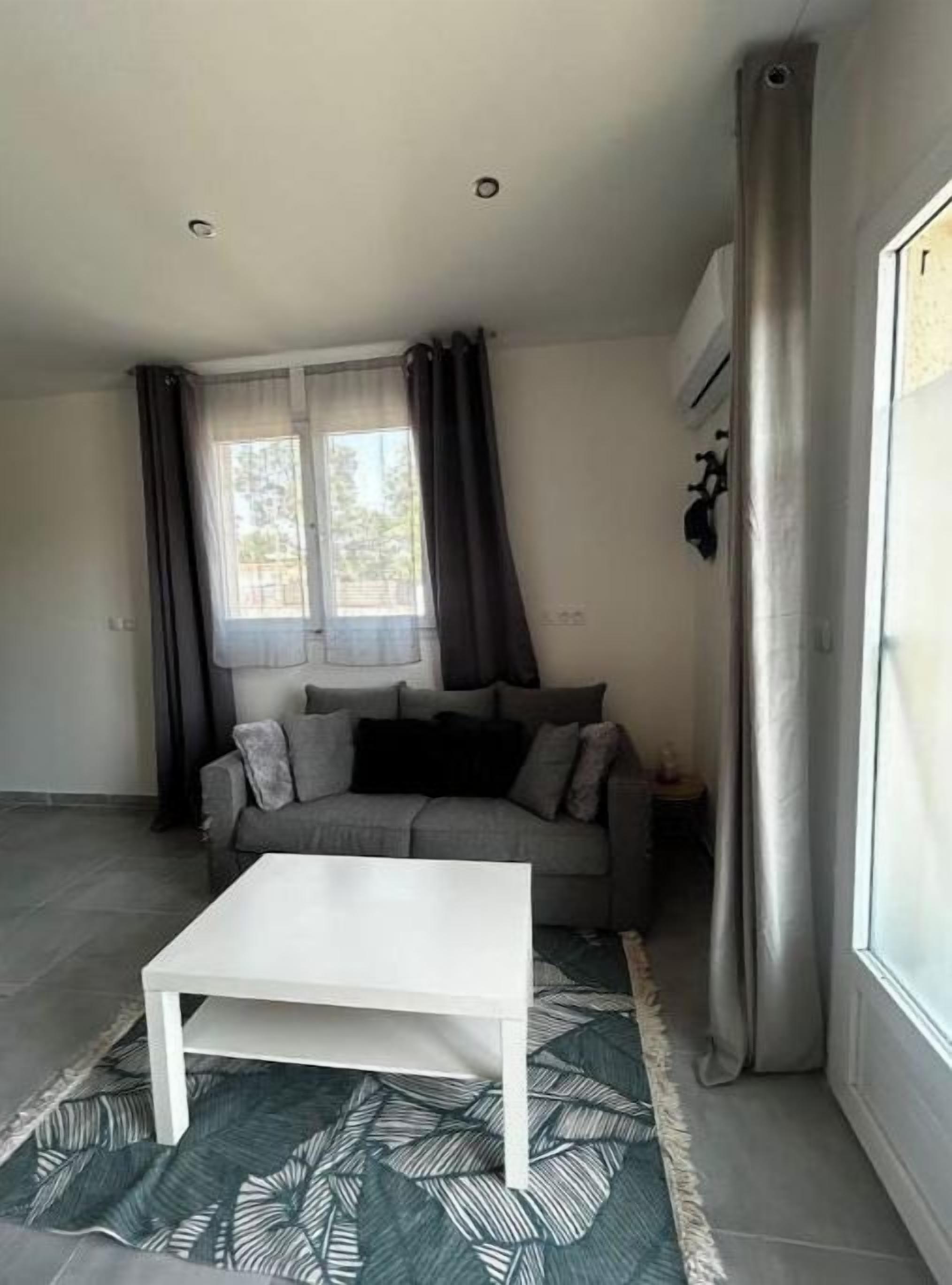 Een woonkamer met een witte salontafel, een grijze bank en een kamerbreed tapijt met dessin.