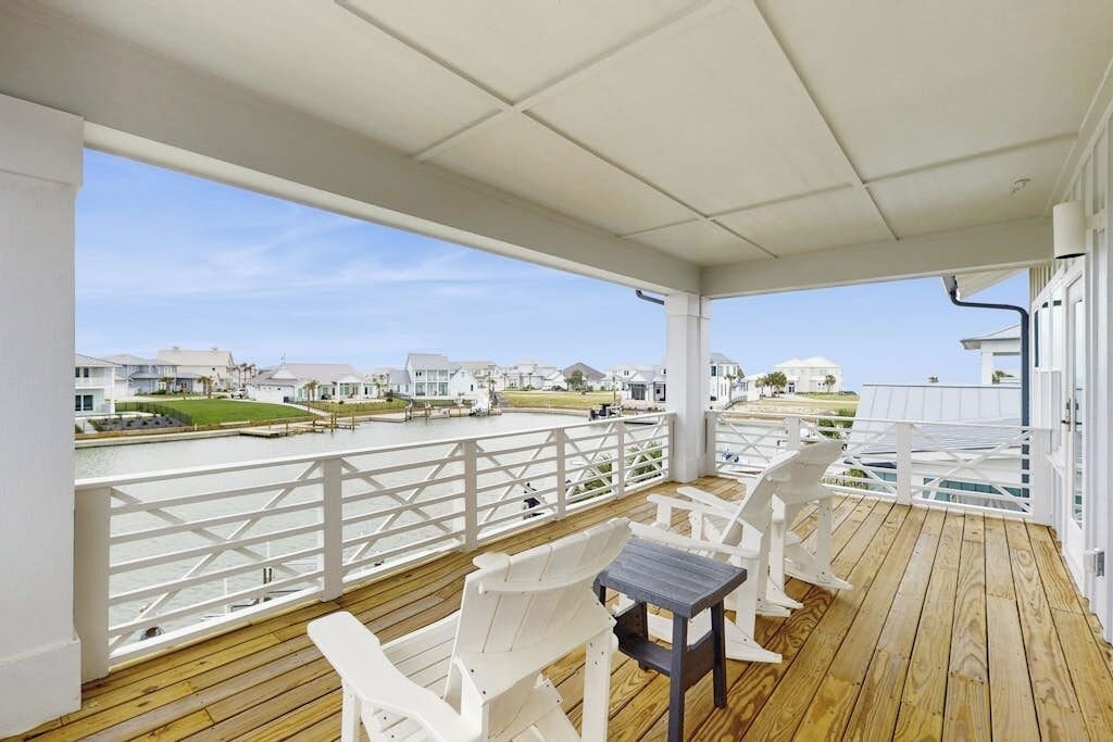 A covered outdoor area with a wooden deck, white chairs, and a table.