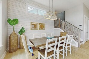 Ein Essbereich mit einem Holztisch und weißen Stühlen, einer hängenden Leuchte und einer Treppe, die in ein Obergeschoss führt.