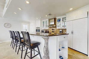A kitchen with white cabinetry, a central island with bar stools, and a clock on the wall. - Saltwater Solace - Under New Ownership (Rockport)