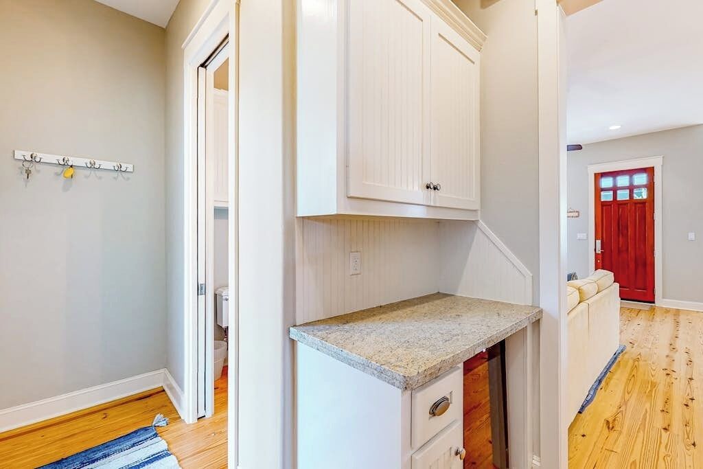 Una cocina con gabinetes blancos, encimera de granito y suelo de madera.
