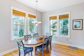 A dining room with a wooden table and chairs, large windows with blinds, a chandelier, and a framed picture on the wall. - Bay Dream Believer - Ocean Views & Shared Pool (Rockport)