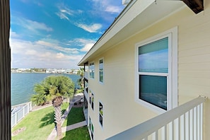 A building with a balcony overlooking a body of water, a clear sky, and a well-maintained lawn with palm trees. - Sand Dollar Unit C3 - Bay Views & Dog-Friendly (Rockport)