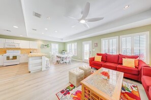 A spacious living area with a red sofa, a coffee table, and a kitchen in the background. - Another Tequila Sunrise (Rockport)