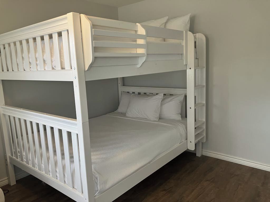 A bunk bed with white bedding in a room with wooden flooring and light-colored walls.