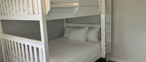 A bunk bed with white bedding in a room with wooden flooring and light-colored walls.