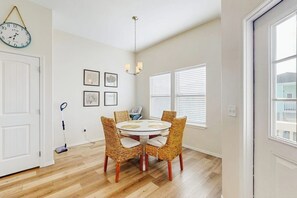 A dining area with a round table and wicker chairs, a clock on the wall, and a chandelier. - Sunrise Retreat - Pool, Minutes to Beach & Golf (Rockport)