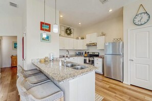 A modern kitchen with a granite countertop, stainless steel appliances, and a large island with bar stools. - Sunrise Retreat - Pool, Minutes to Beach & Golf (Rockport)