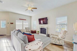 A living room with a sofa, armchair, fireplace, television, and a ceiling fan. - Sunrise Retreat - Pool, Minutes to Beach & Golf (Rockport)