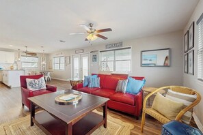 A spacious living area with a red sofa, a wooden coffee table, and a wicker chair. A ceiling fan is visible, and there are framed pictures on the wall. - Salt Lake Lodge - Bayfront, Big Decks & Yard (Rockport)