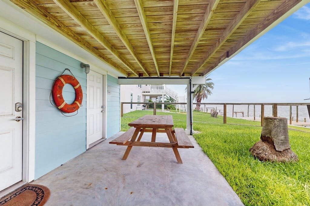 Un porche techado con una mesa de picnic, un flotador en la pared y vista a la playa.