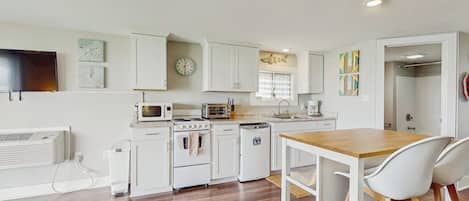 Una cocina moderna con armarios blancos, una mesa de comedor de madera y sillas blancas.