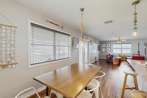 A dining area with a wooden table and white chairs, a kitchen in the background, and a ceiling fan. - Salt Lake Lodge - Bayfront, Big Decks & Yard (Rockport)
