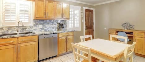 A kitchen with wooden cabinets, a dishwasher, a tiled backsplash, and a dining area with a table and chairs.