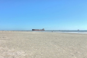 A sandy beach with a large cargo ship in the distance. - Nelray Shores at Seamist Condominiums (Port Aransas)