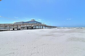 A beach with a pier extending into the ocean, a building on the pier, and a clear sky. - Nelray Shores at Seamist Condominiums (Port Aransas)